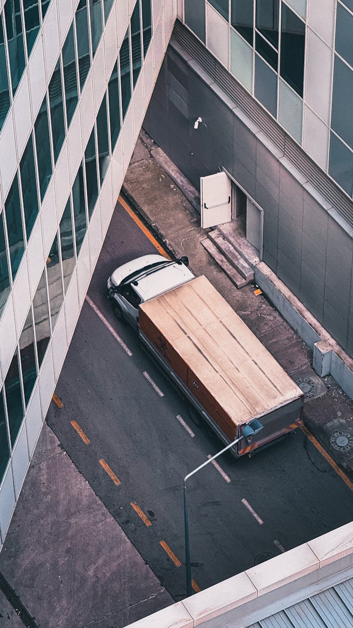 Aerial perspective of a truck navigating a city alley between modern buildings.